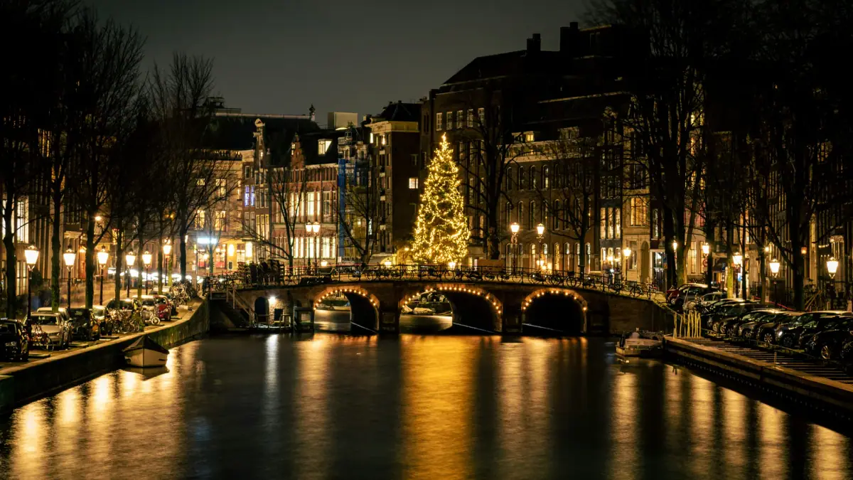 Een kerstboom en verlichte brug weerspiegelen in een Amsterdamse gracht in het donker