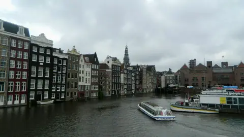 A covered canal boat on the Damrak in Amsterdam beneath cloudy skies