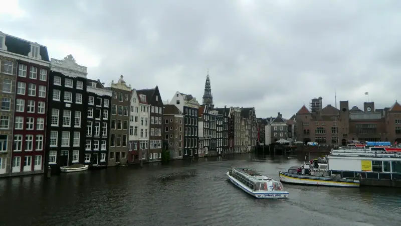 A covered canal boat on the Damrak in Amsterdam beneath cloudy skies