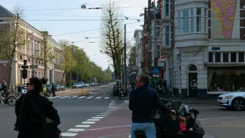 Ouders fietsen met kinderen in bakfietsen door een Amsterdamse straat