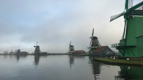 Windmills reflected in the water at Zaanse Schans under a misty grey sky