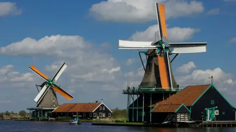 Traditional Dutch windmills with orange sails beside the water at Zaanse Schans on a sunny day