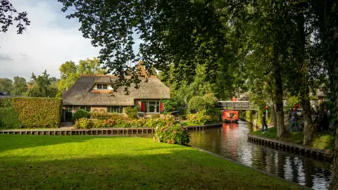 Thatched farmhouse, wooden bridge and boat beside a canal in Giethoorn