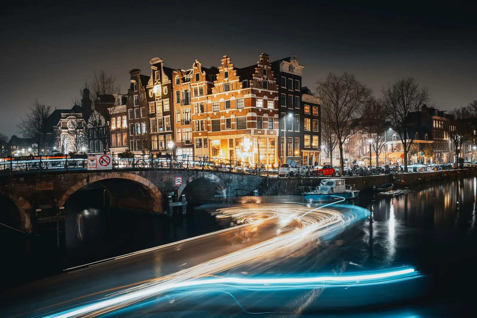 Amsterdam canal houses lit up at night with light trails on the water
