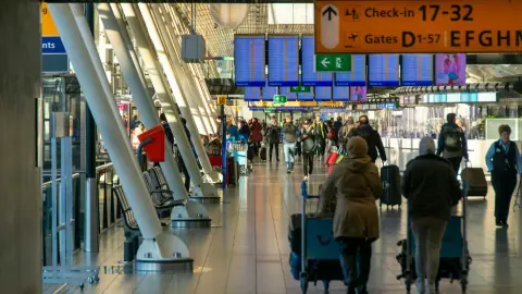 Travellers with luggage trolleys under the departure boards and yellow signs at Schiphol airport