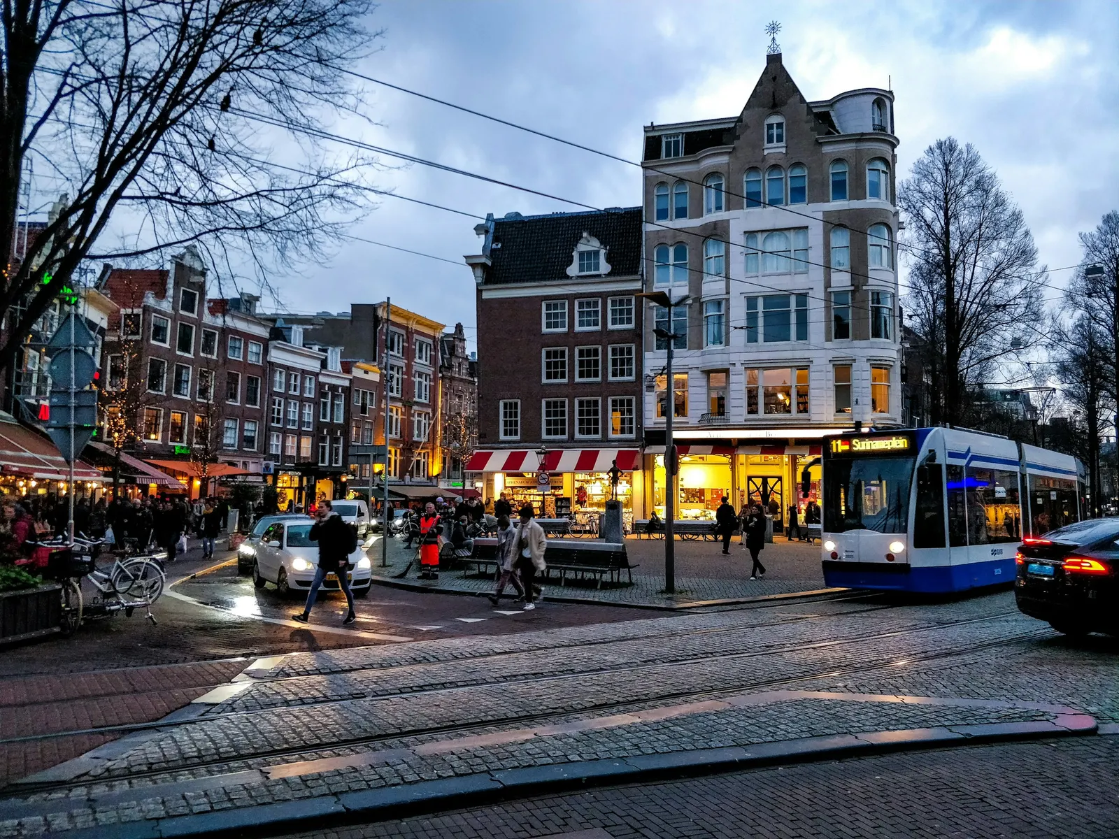 Tram passeert een verlicht plein in de schemering in het centrum van Amsterdam