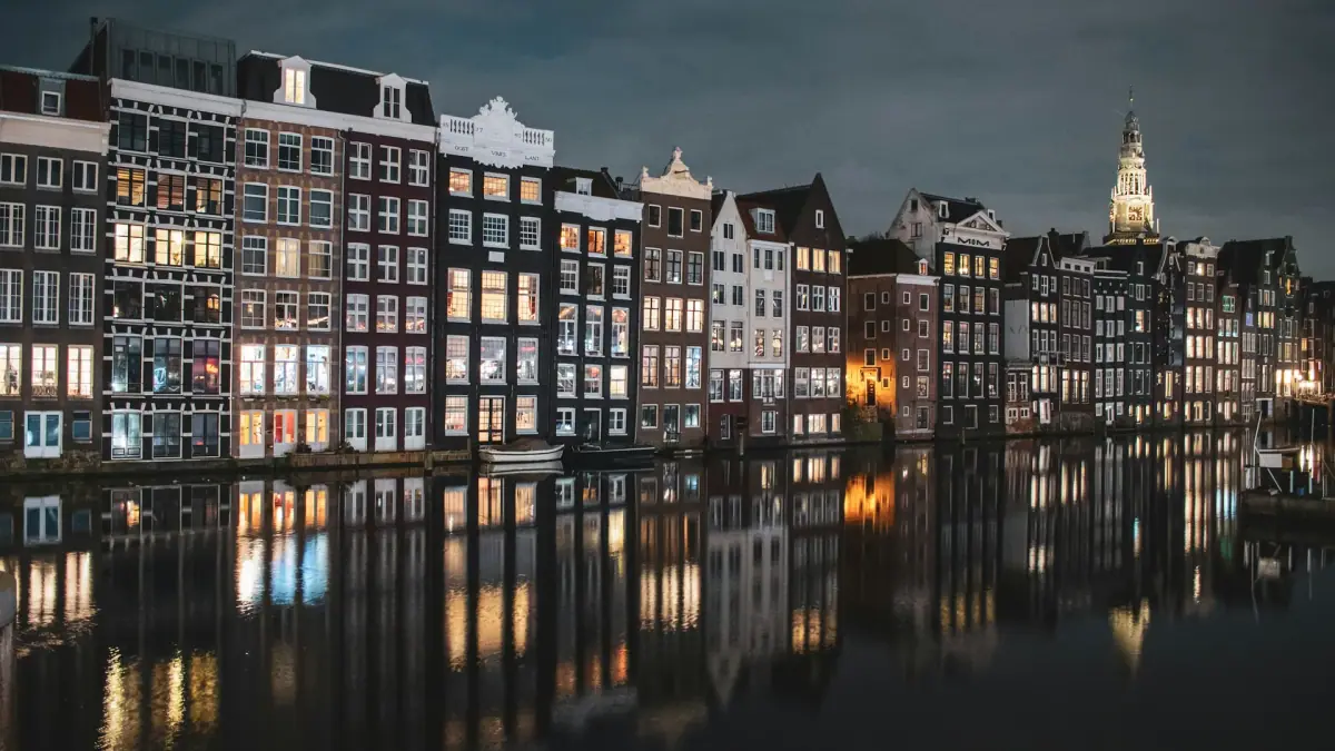 Grachtenpanden aan het Damrak verlicht in de nacht en weerspiegeld in het water, Amsterdam