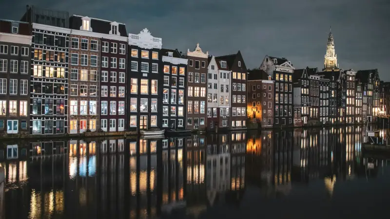 Canal houses on the Damrak lit up at night and reflected in the water, Amsterdam