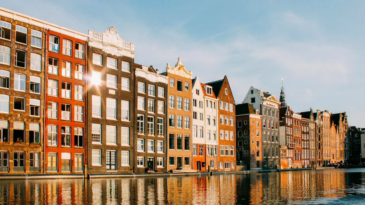 Gabled canal houses on the Damrak in Amsterdam glowing in late afternoon sun, reflected in the water