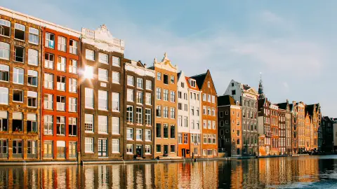Gabled canal houses on the Damrak in Amsterdam glowing in late afternoon sun, reflected in the water