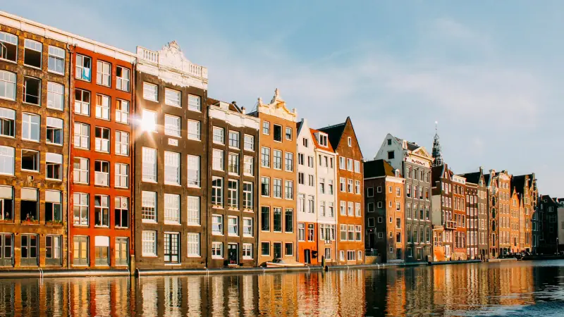 Gabled canal houses on the Damrak in Amsterdam glowing in late afternoon sun, reflected in the water