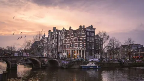 Historic Amsterdam canal houses and a bridge under a pink evening sky