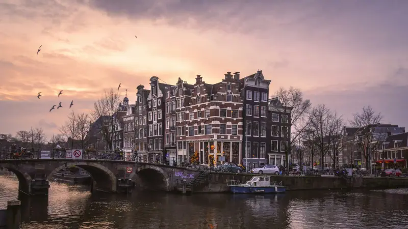 Historic Amsterdam canal houses and a bridge under a pink evening sky